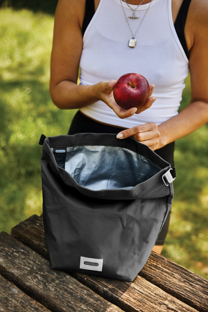 Personne tenant une pomme devant un sac isotherme.