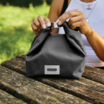 Personne fermant un sac repas noir sur table en bois
