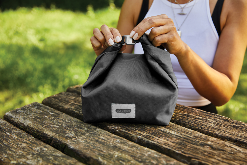 Personne fermant un sac repas noir sur table en bois
