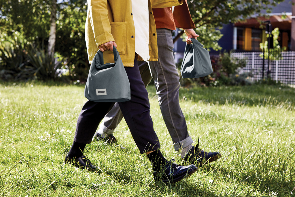 Deux personnes marchent avec des sacs gris.