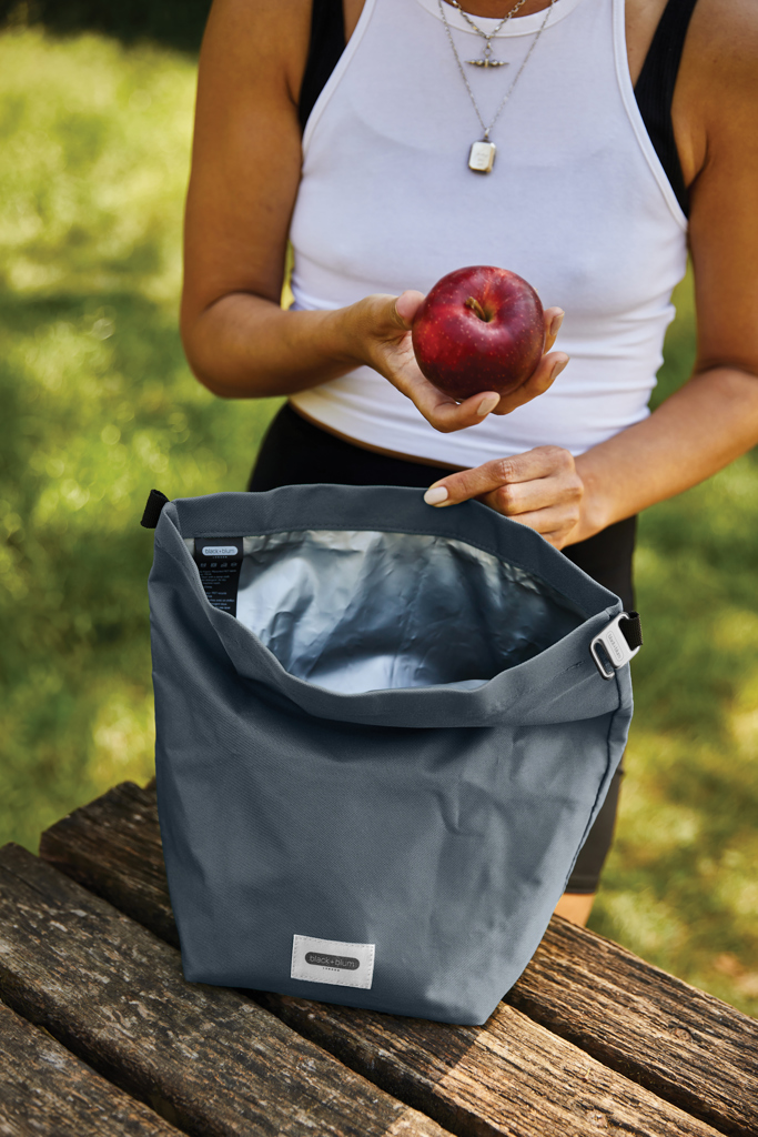 Personne tenant une pomme près d’un sac isotherme.