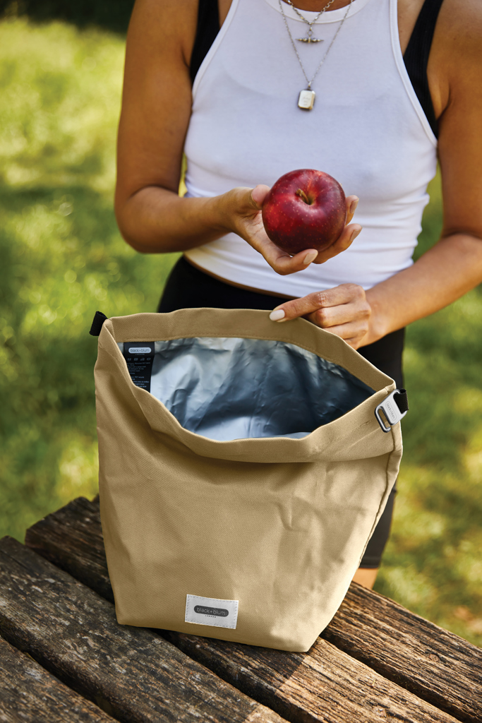 Personne tenant une pomme près d’un sac isotherme beige.