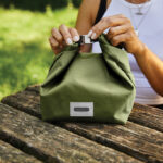 Personne fermant un sac isotherme vert sur table.