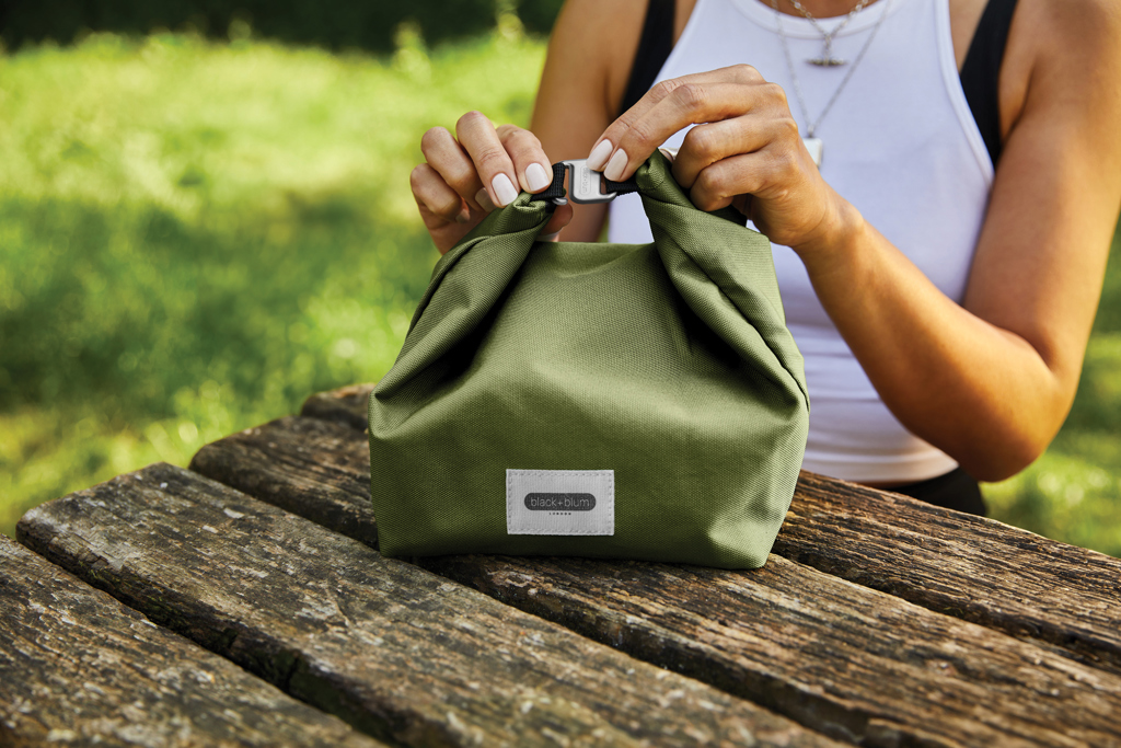 Personne fermant un sac isotherme vert sur table.
