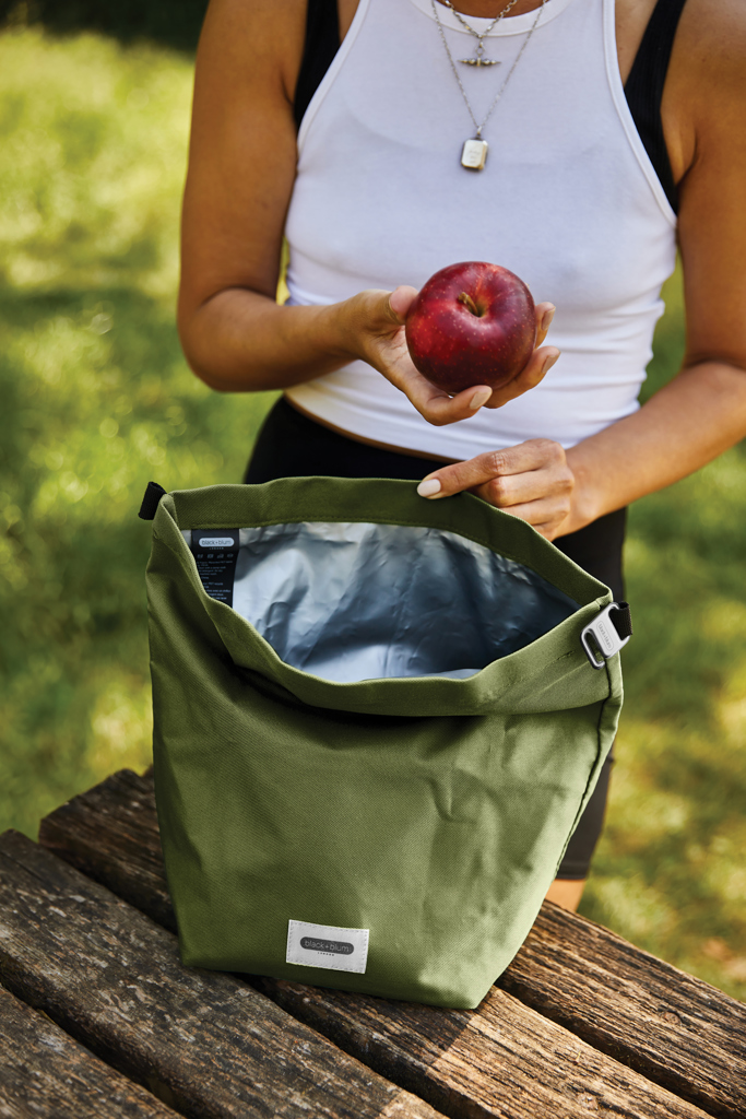 Personne tenant une pomme près d’un sac vert.