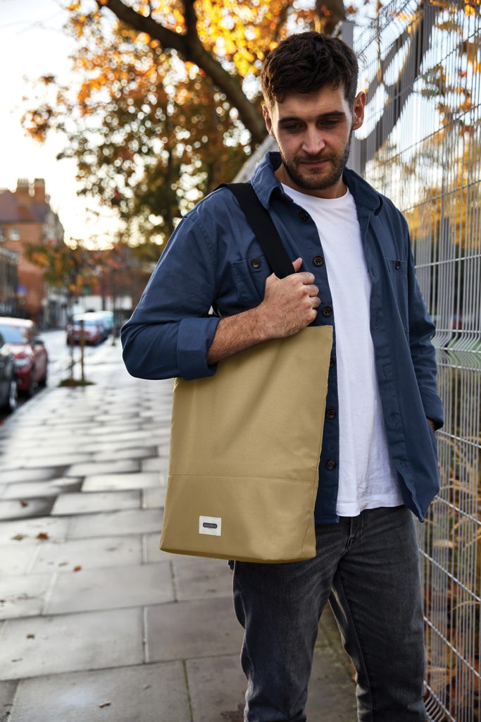 Homme portant un grand sac beige en ville