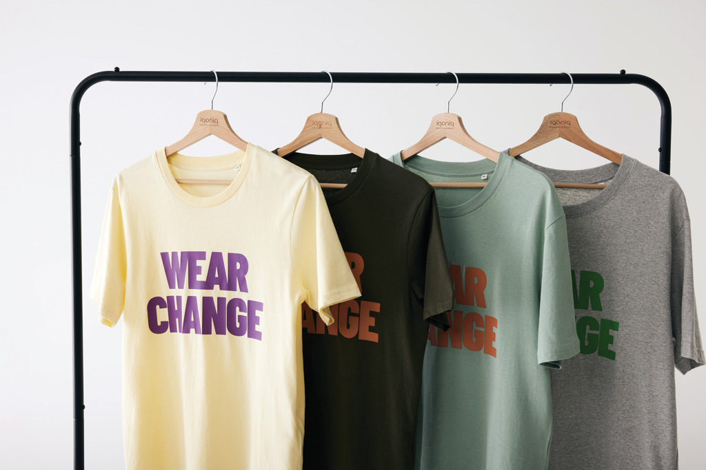 Quatre t-shirts colorés suspendus sur un portant.