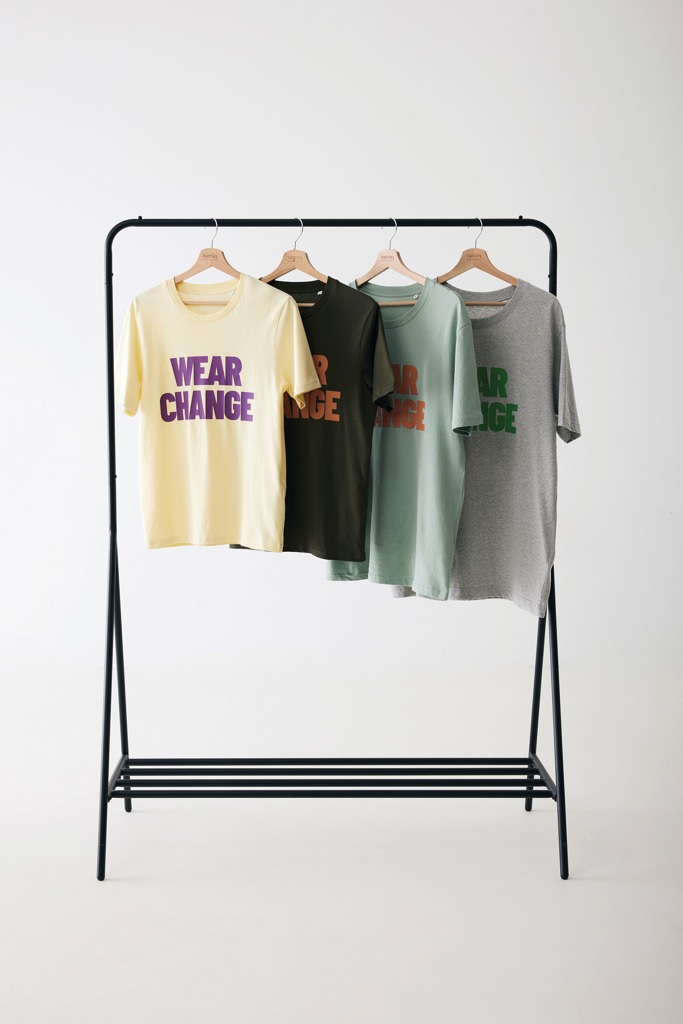 Quatre t-shirts colorés suspendus sur un portant.