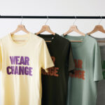 Quatre t-shirts colorés suspendus sur un portant.