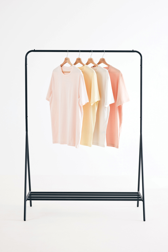 Quatre t-shirts pastel suspendus sur un portant noir