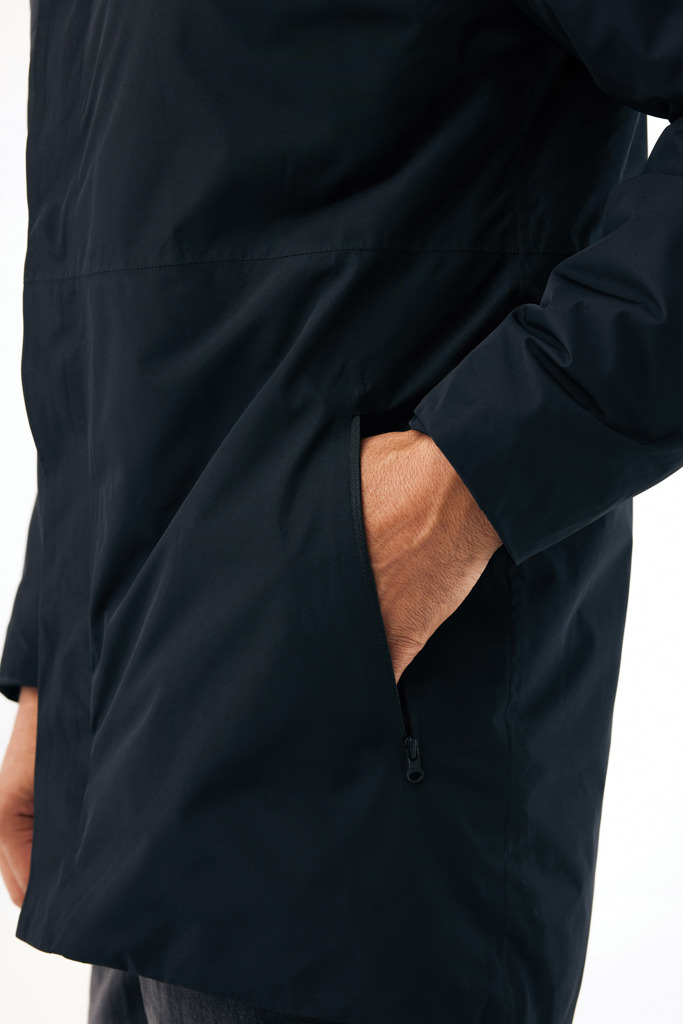 Main dans la poche d’une veste noire.