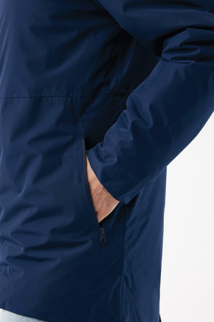 Main dans la poche d’un manteau bleu marine.