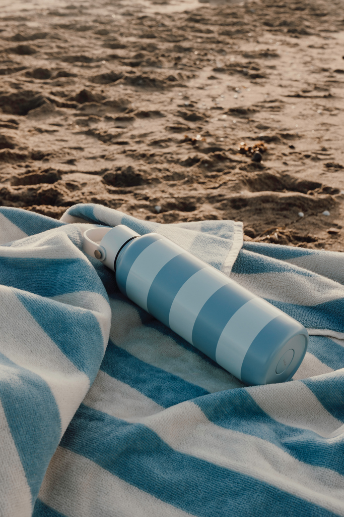 Gourde bleue sur serviette rayée à la plage