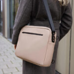 Sac beige porté à l'épaule sur manteau gris.
