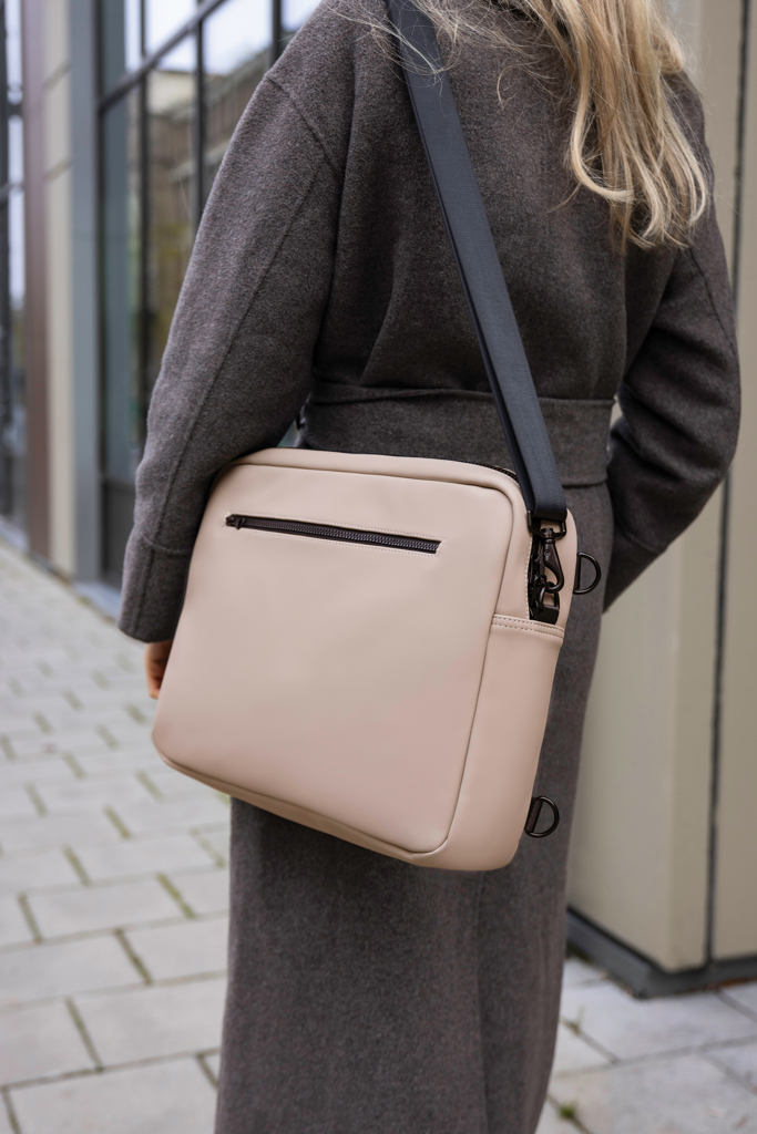 Sac beige porté à l'épaule sur manteau gris.