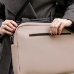 Sac beige porté en bandoulière sur manteau gris.