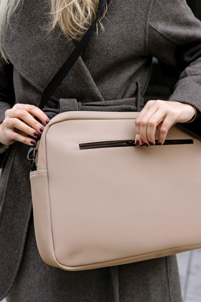 Sac beige porté en bandoulière sur manteau gris.
