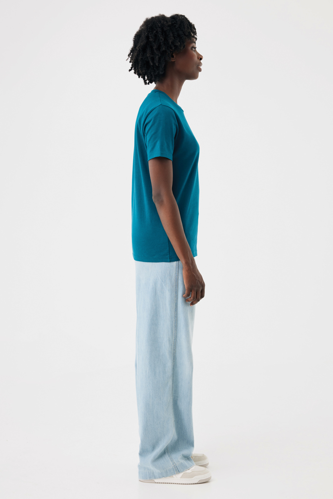 Femme de profil en t-shirt turquoise et jean
