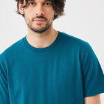 Homme aux cheveux mi-longs en t-shirt bleu pétrole