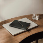 Ordinateur portable, carnet noir et verre d’eau